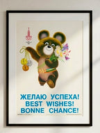 Framed Moscow Olympics poster with a cartoon bear holding flowers and Olympic rings, text in multiple languages.