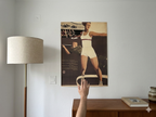 Person adjusting a vintage-style poster on a wall next to a lamp and books.