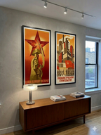 Two framed propaganda posters on a wall above a wooden console table.