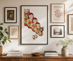 Wall with framed artwork including a colorful Russian doll print, a plant, and books on a wooden surface.