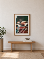 Framed artwork on a wall above a wooden bench in a room with a plant and books.