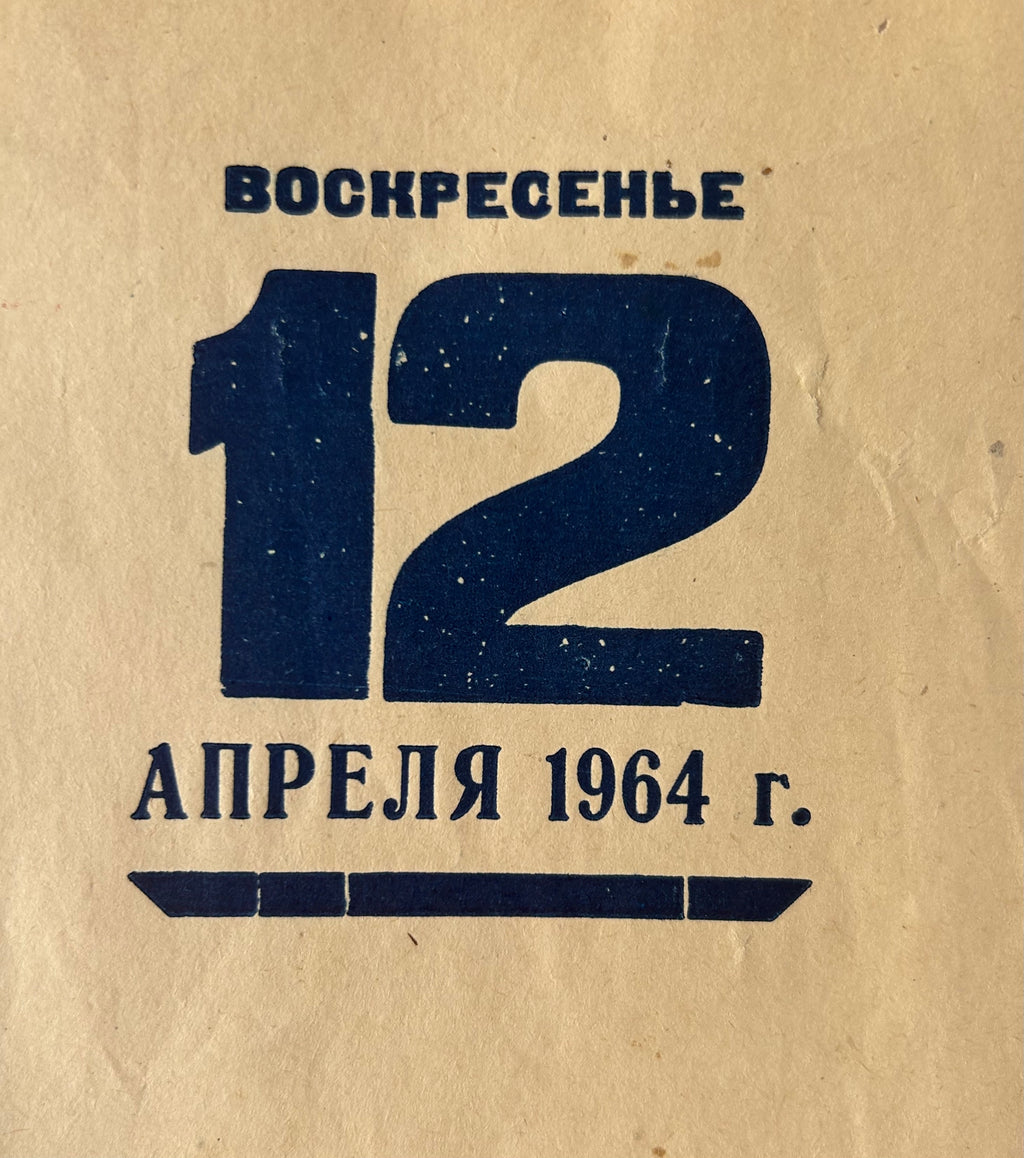 A close-up of a vintage paper item, likely a book cover or album sleeve, printed with Russian text 'ВОСКРЕСЕНЬЕ 12 АПРЕЛЯ 1964 г.' in dark blue ink on a textured beige background.