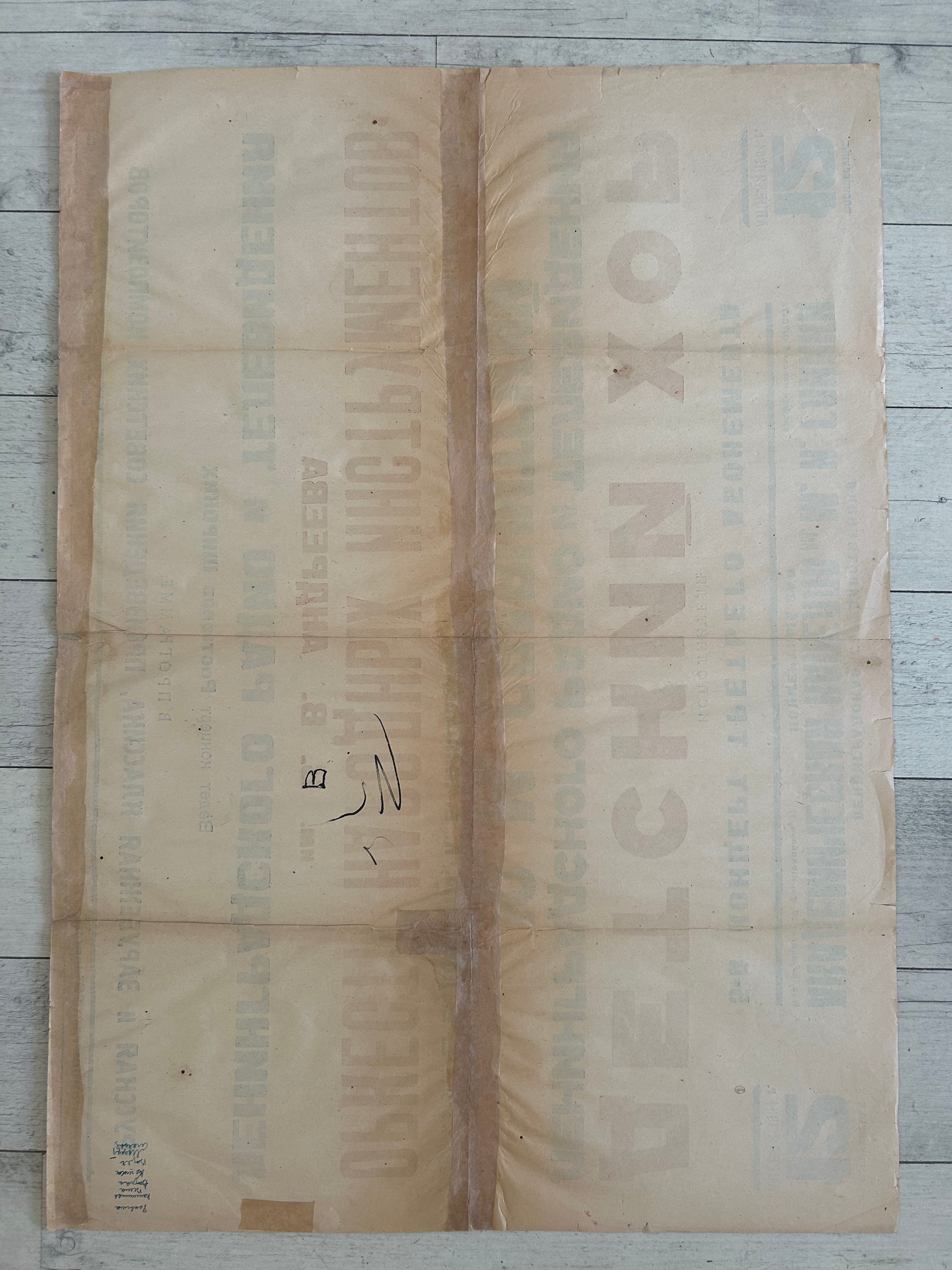 A vintage Russian paper poster or advertisement with faded text, laid flat on a light gray wooden surface.