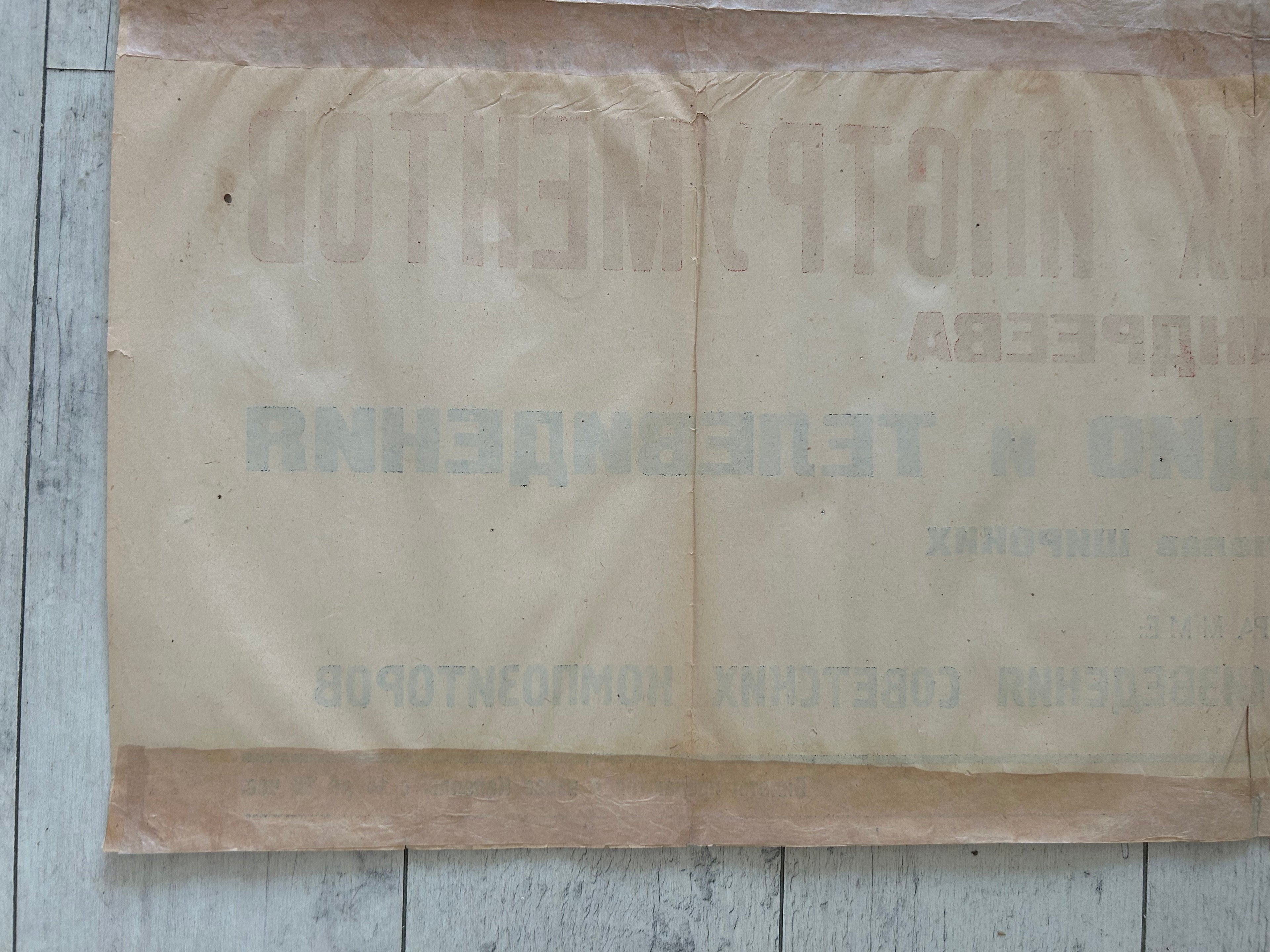 A vintage beige paper banner or sign with faded Cyrillic text, laid flat on a light-colored wooden surface.