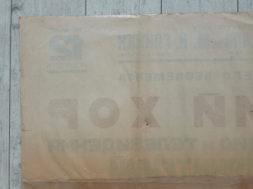 A vintage beige paper label or packaging sheet with faded Cyrillic text, laid flat on a light gray wood plank surface.