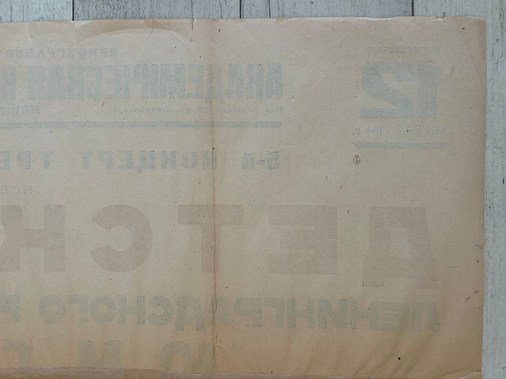 A vintage beige paper document or poster with faded Cyrillic text, laid flat on a light gray wooden surface.
