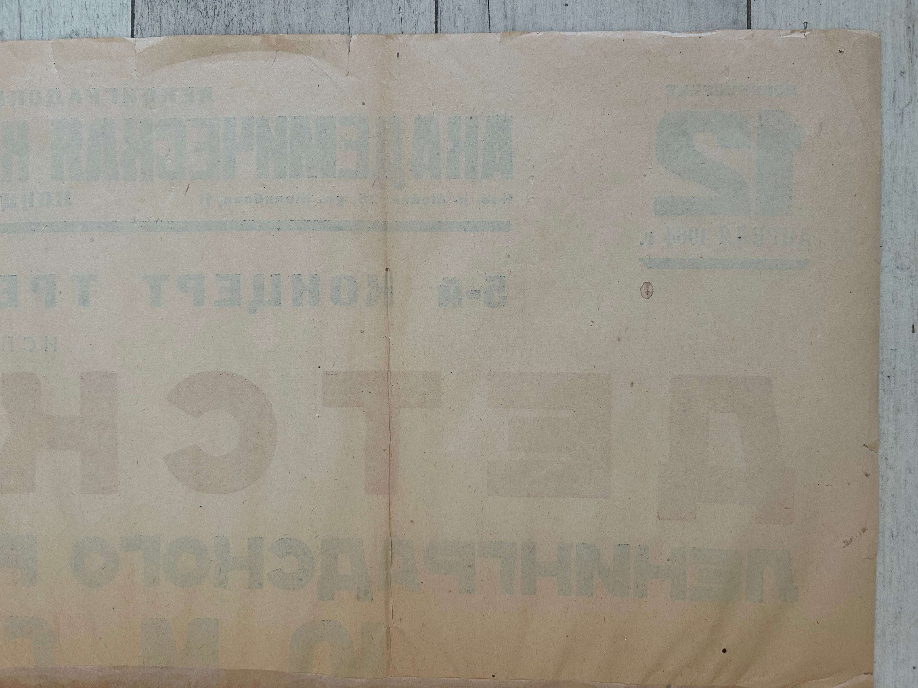 A vintage beige paper document or poster with faded Cyrillic text, laid flat on a light gray wooden surface.