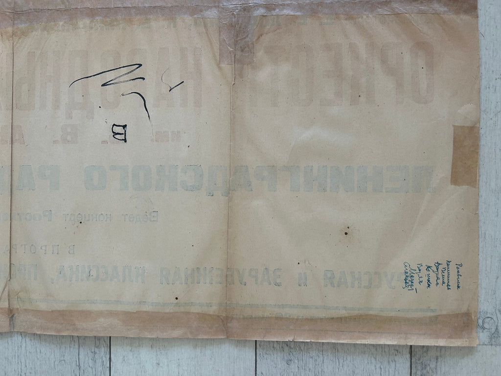 A vintage beige paper envelope or document with faded blue Cyrillic text and a black handwritten mark, laid flat on a light wood surface.