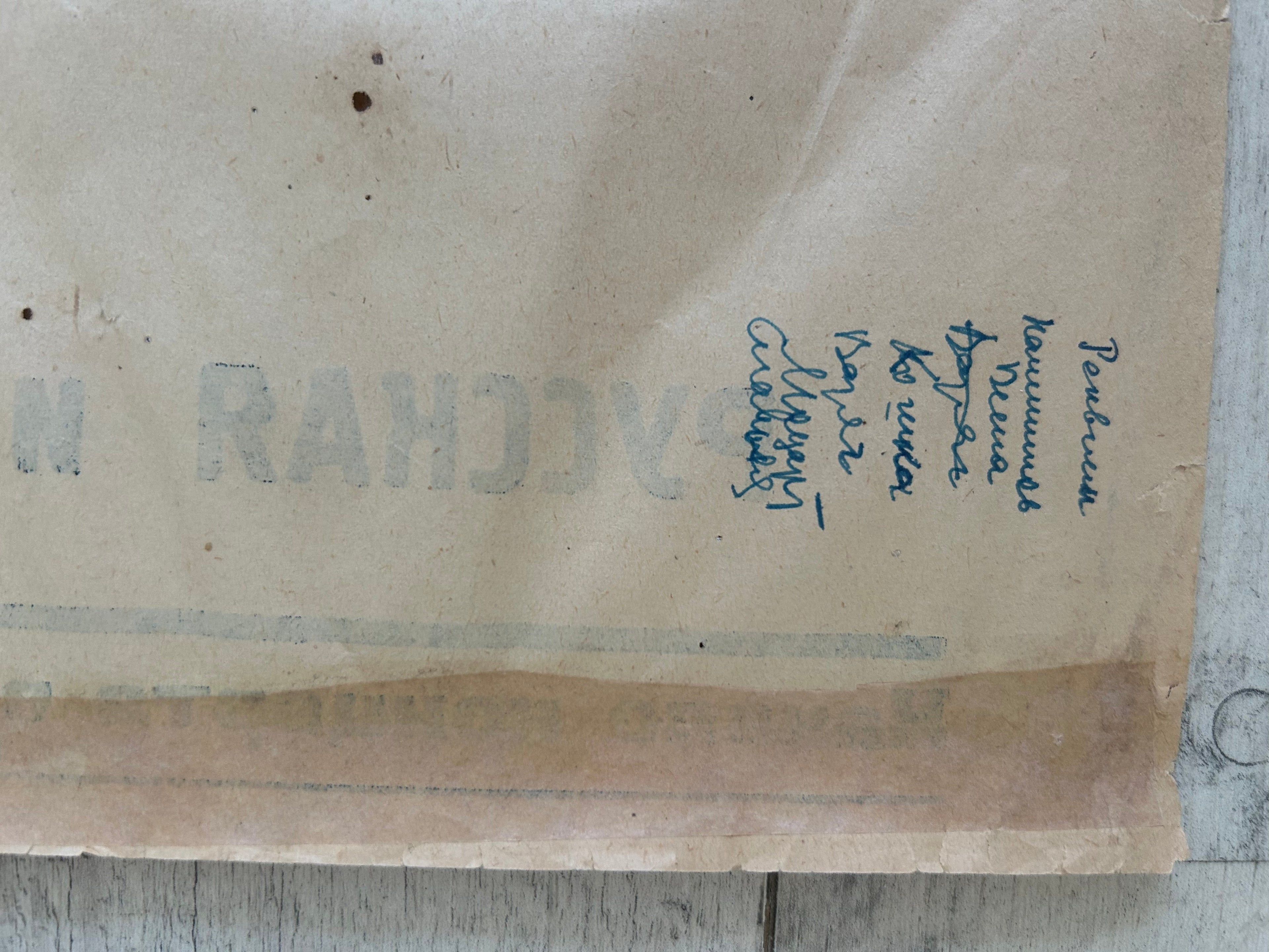 A close-up of a vintage, aged beige paper envelope or letterhead with blue handwritten address text on the right side and faint gray stamped text on the left.