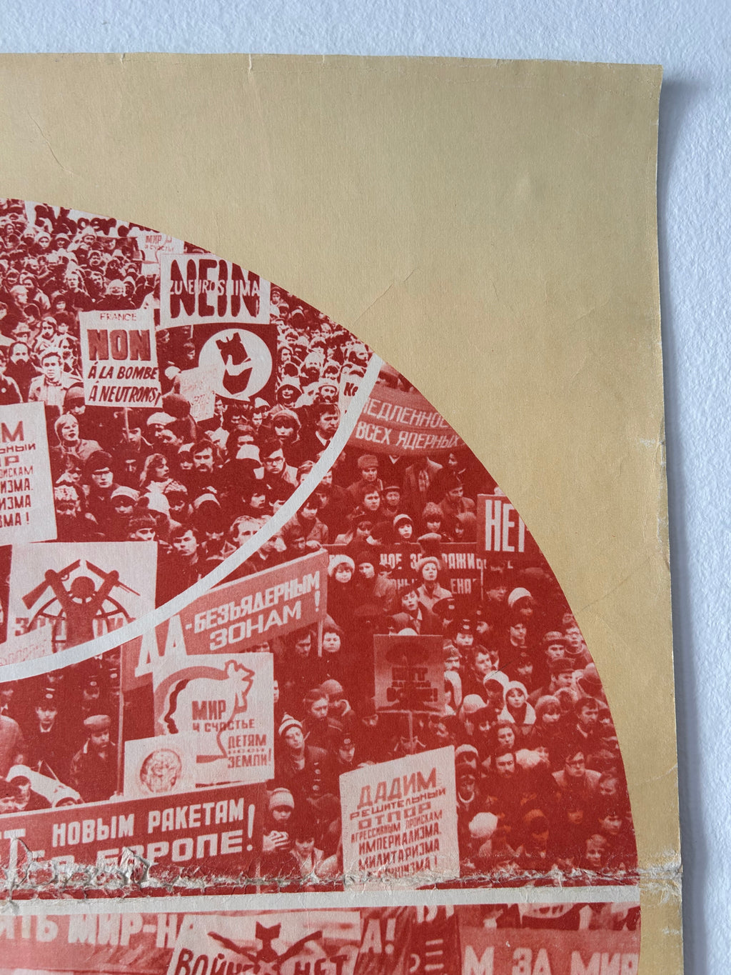 A close-up of a printed textile or poster-like product showing a collage of red and beige imagery with Cyrillic text and protest-style signs, photographed against a light blue background.