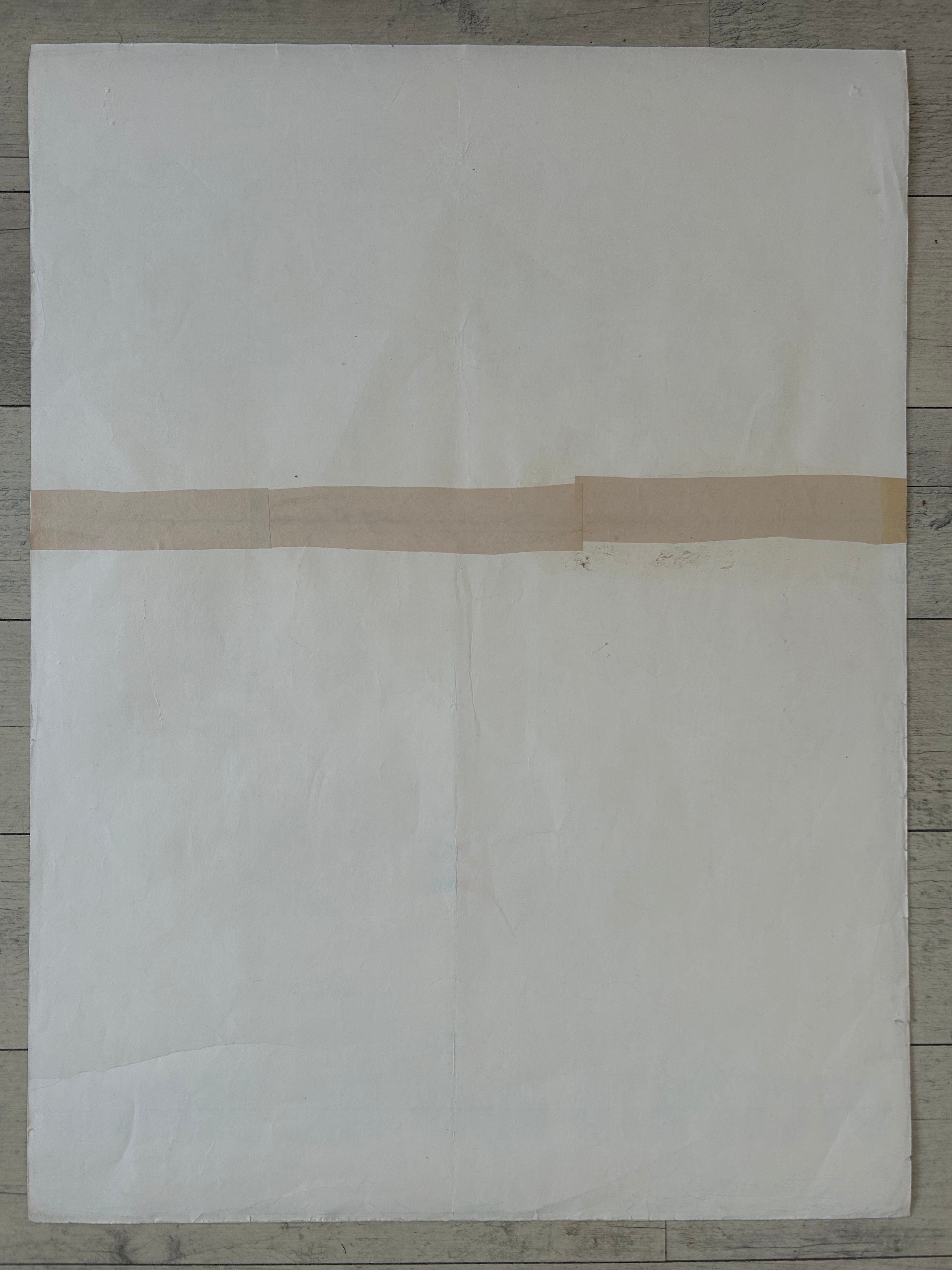 A large off-white sheet of paper or fabric laid flat on a gray wood floor, with a narrow beige tape strip crossing horizontally across the middle.