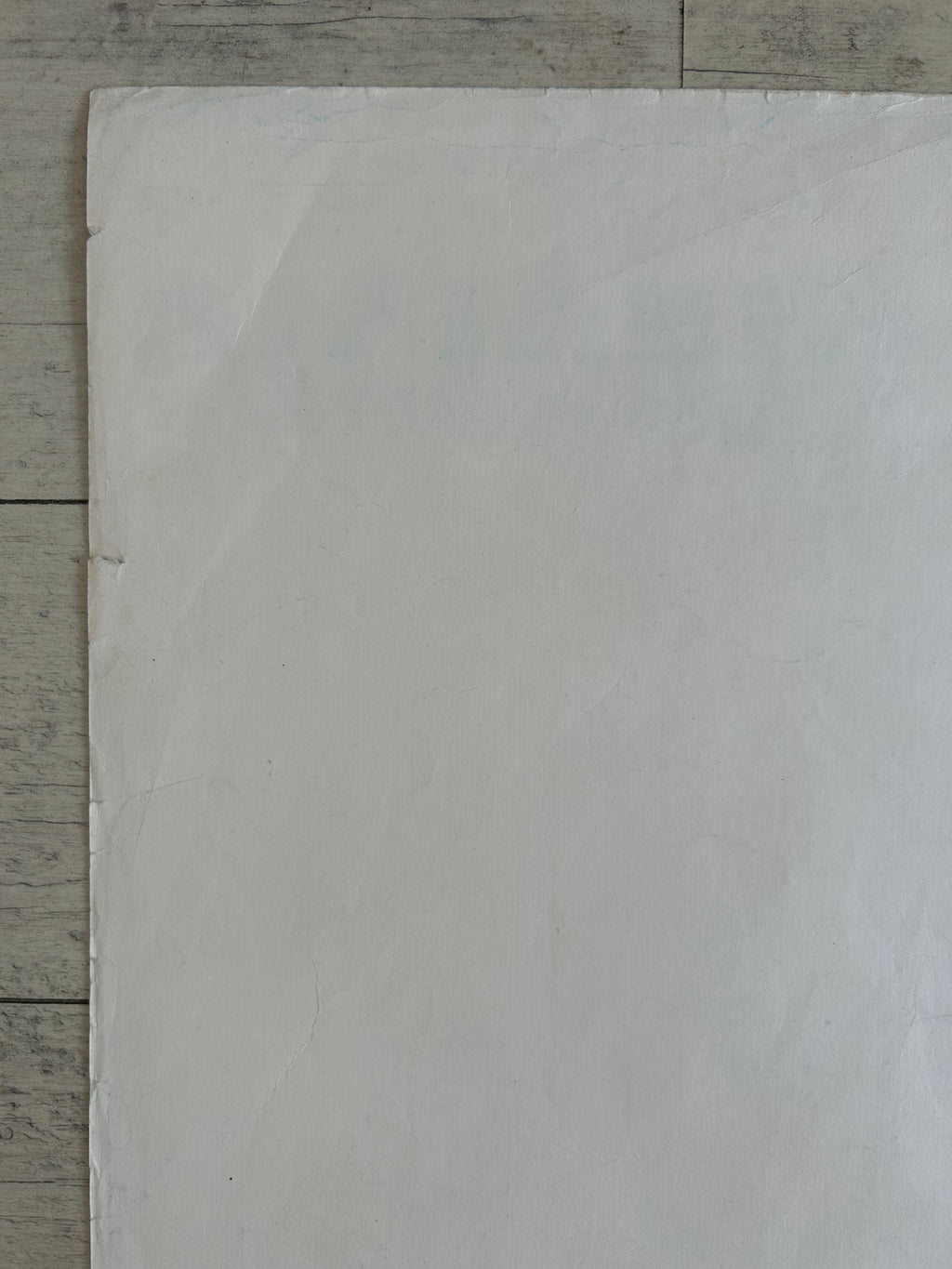 A large blank white sheet of paper or cardstock laid flat on a light gray wood-grain surface.