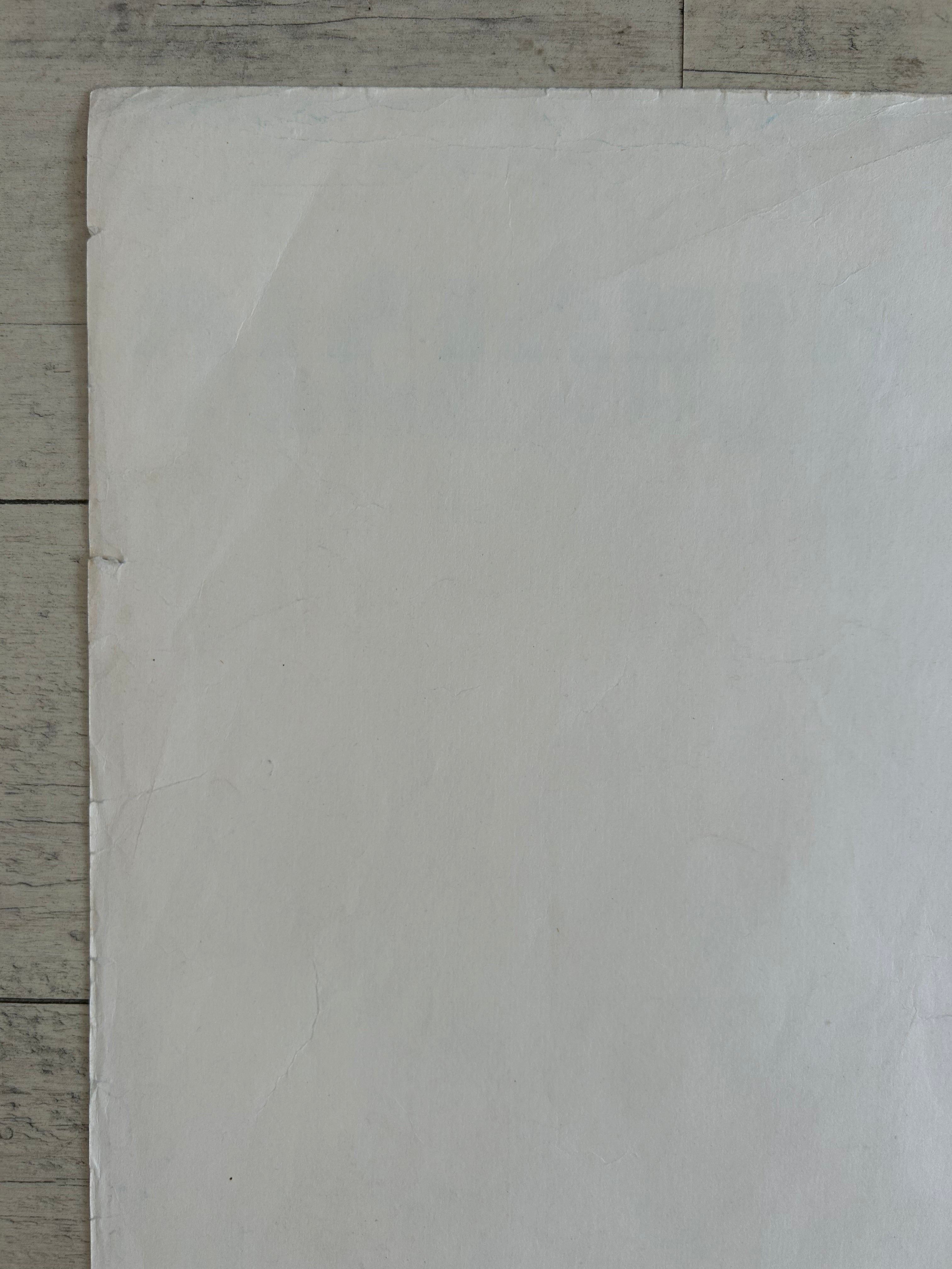 A large blank white sheet of paper or cardstock laid flat on a light gray wood-grain surface.