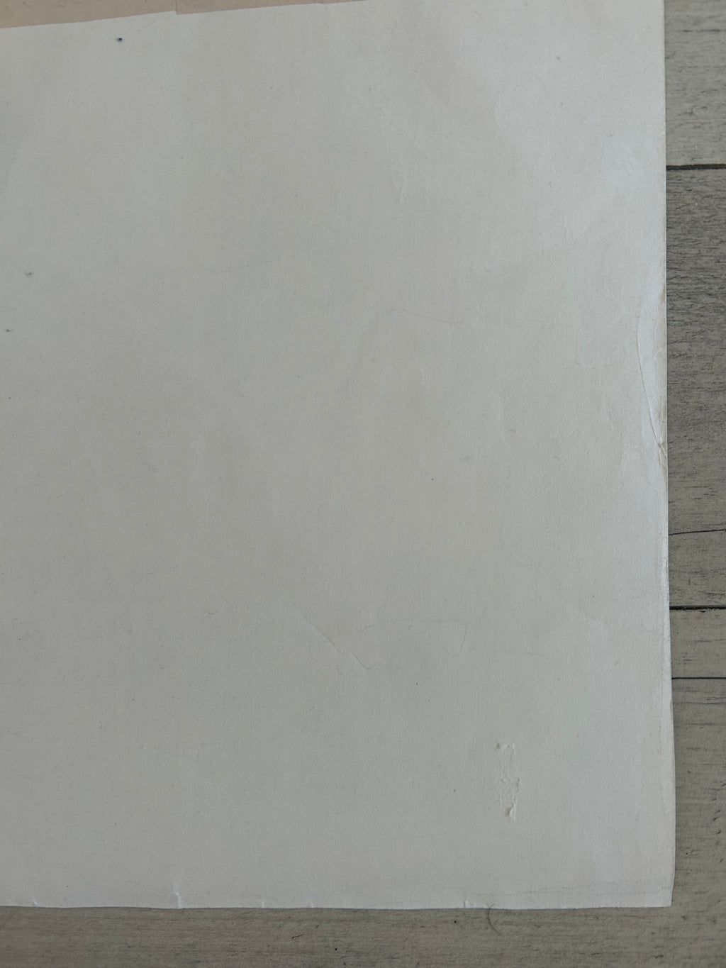 A blank white sheet of paper or cardstock placed on a gray wood-grain surface.