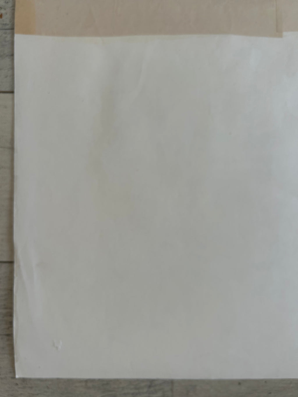 A blank white sheet of paper or cardstock placed on a light-colored wooden surface.