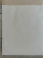 A blank white sheet of paper or cardstock placed on a light-colored wooden surface.