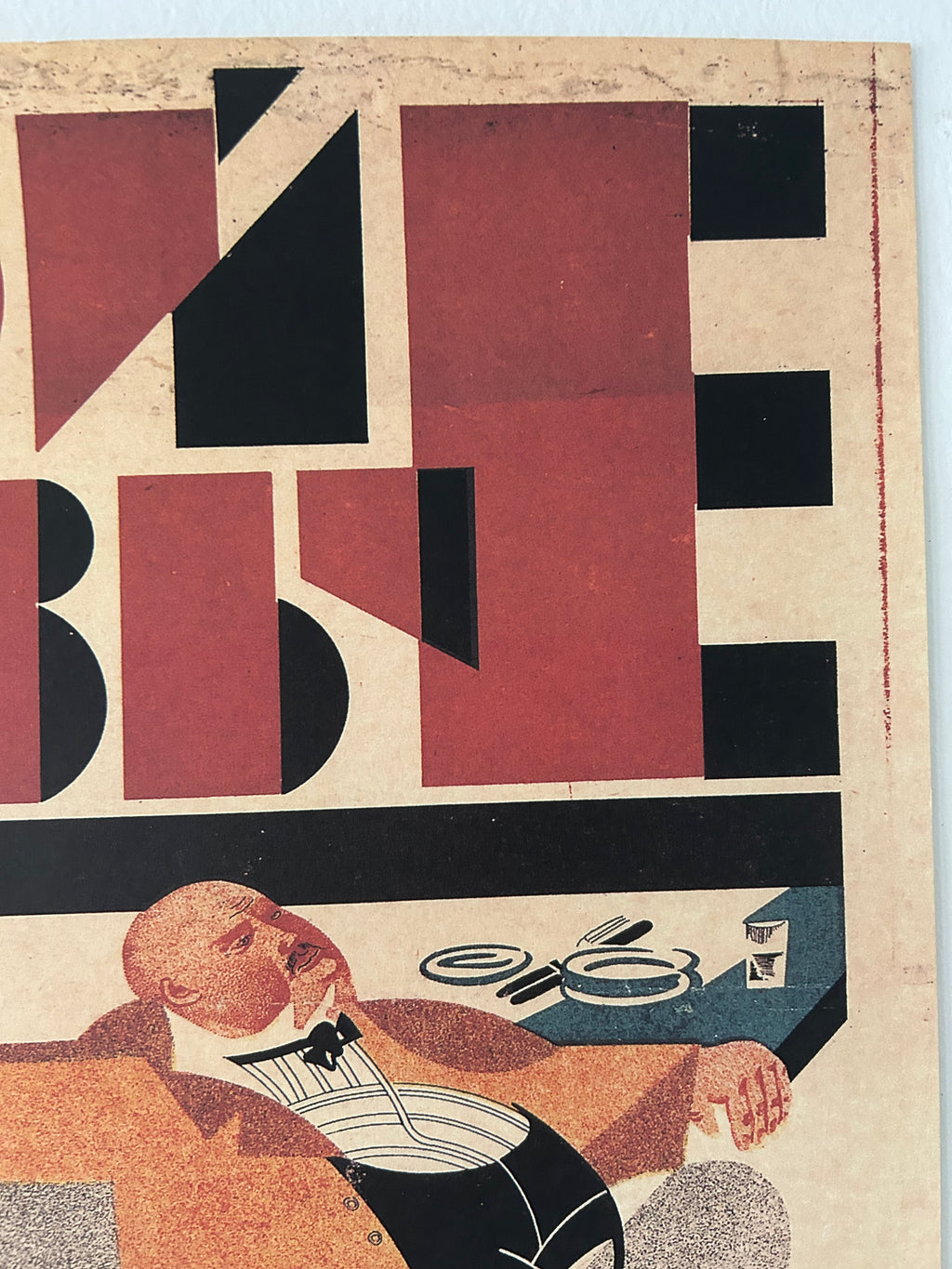 A close-up of an abstract art print featuring geometric shapes in terracotta red, black, and cream, alongside a stylized figure in brown, black, and white.