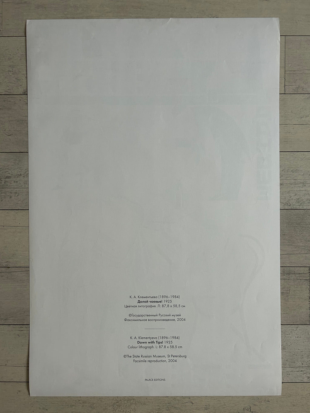 A large white sheet of paper with printed text in the lower right corner, photographed from above on a light wood floor.
