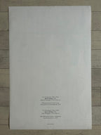 A large white sheet of paper with printed text in the lower right corner, photographed from above on a light wood floor.