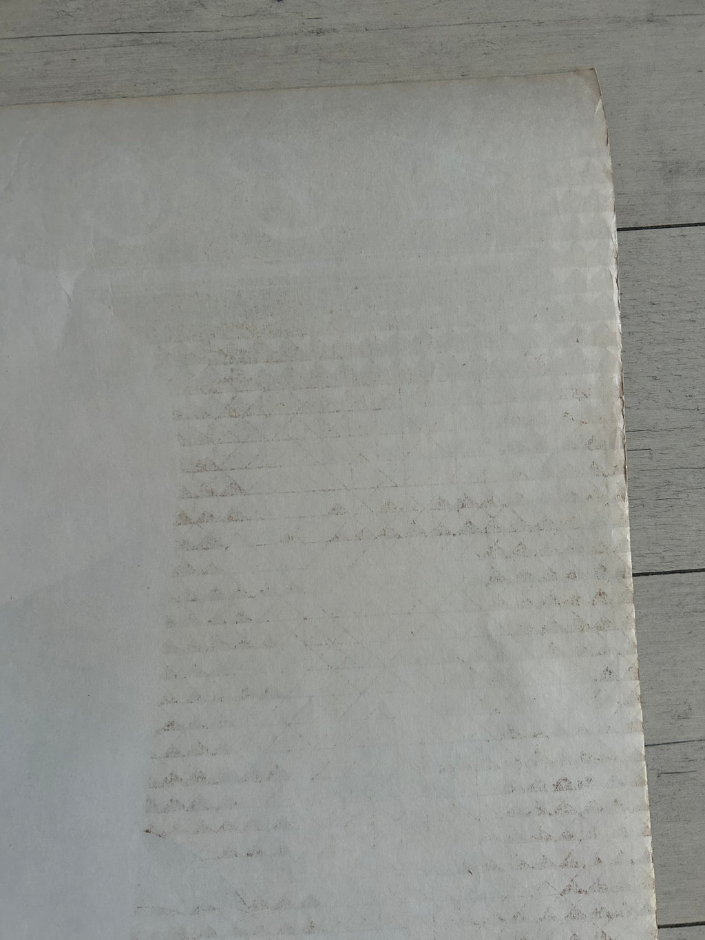 A close-up of a light gray textured material, possibly a foam sheet or textured paper, laid flat against a light gray wood plank background.