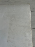 A close-up of a light gray textured material, possibly a foam sheet or textured paper, laid flat against a light gray wood plank background.