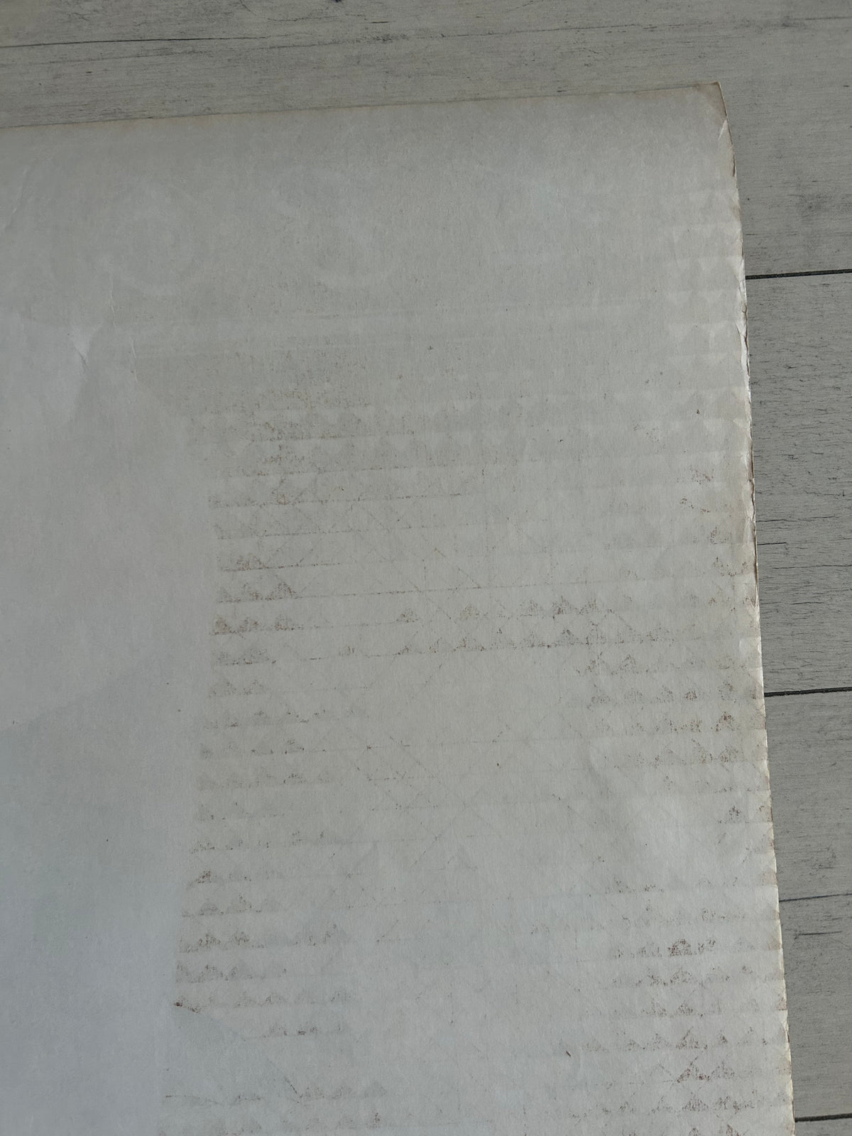 A close-up of a light gray textured material, possibly a foam sheet or textured paper, laid flat against a light gray wood plank background.
