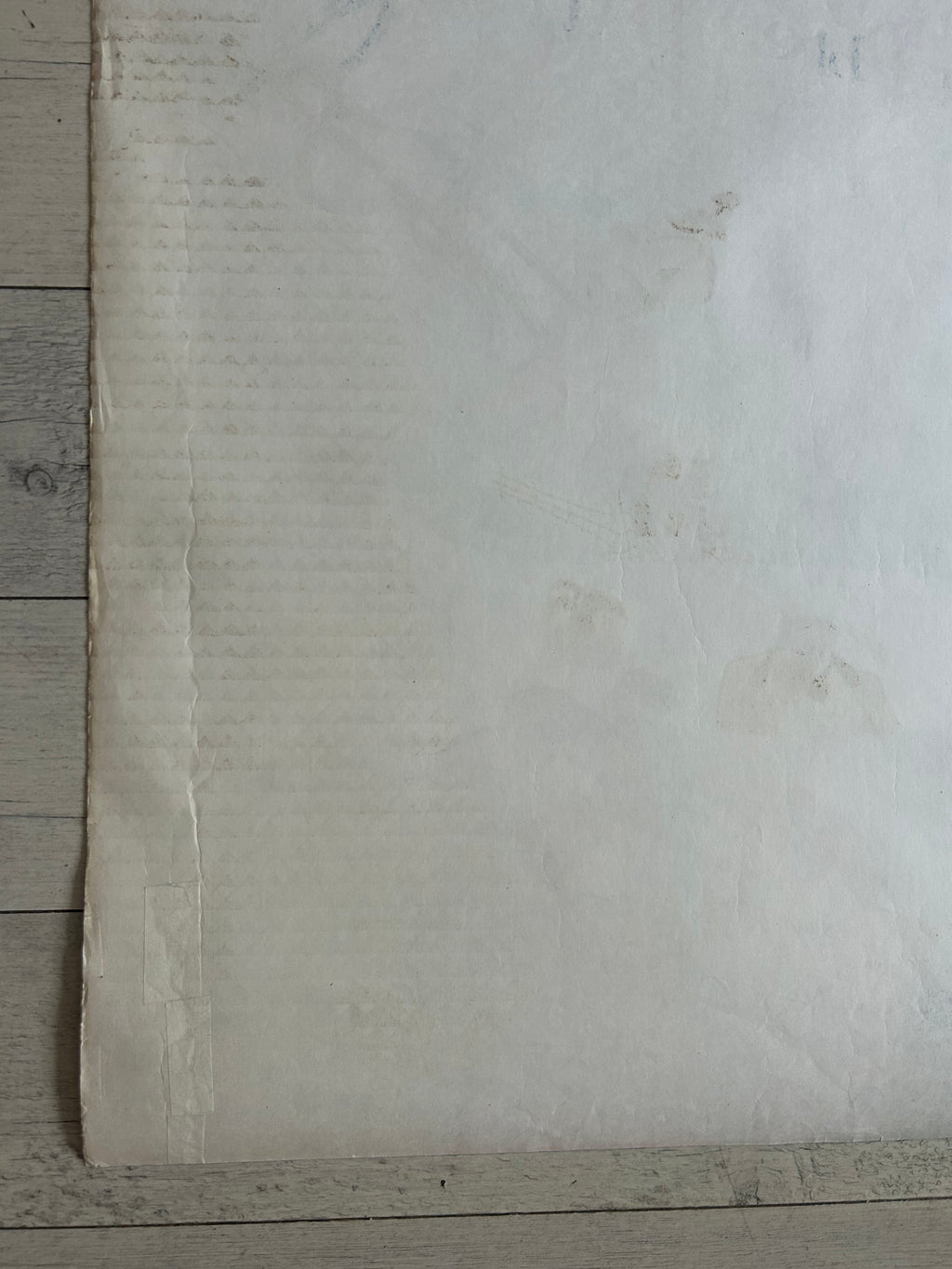 A large off-white sheet of textured paper or fabric laid flat on a light gray wood plank surface.