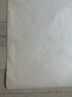 A large off-white sheet of textured paper or fabric laid flat on a light gray wood plank surface.