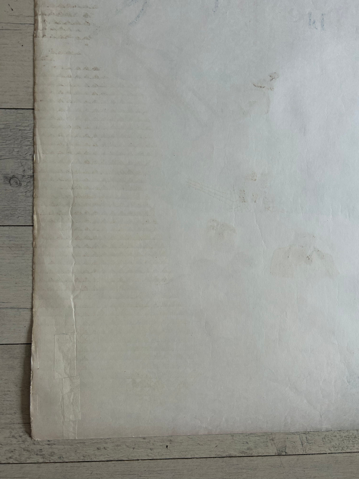 A large off-white sheet of textured paper or fabric laid flat on a light gray wood plank surface.