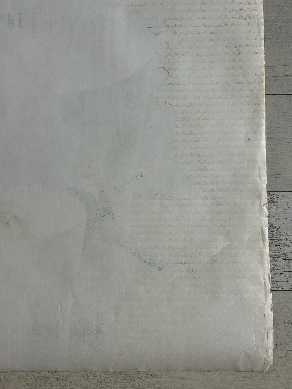 A close-up of a textured, off-white fabric or paper material with a subtle vertical ribbed pattern and faint gray markings, set against a weathered gray wood background.