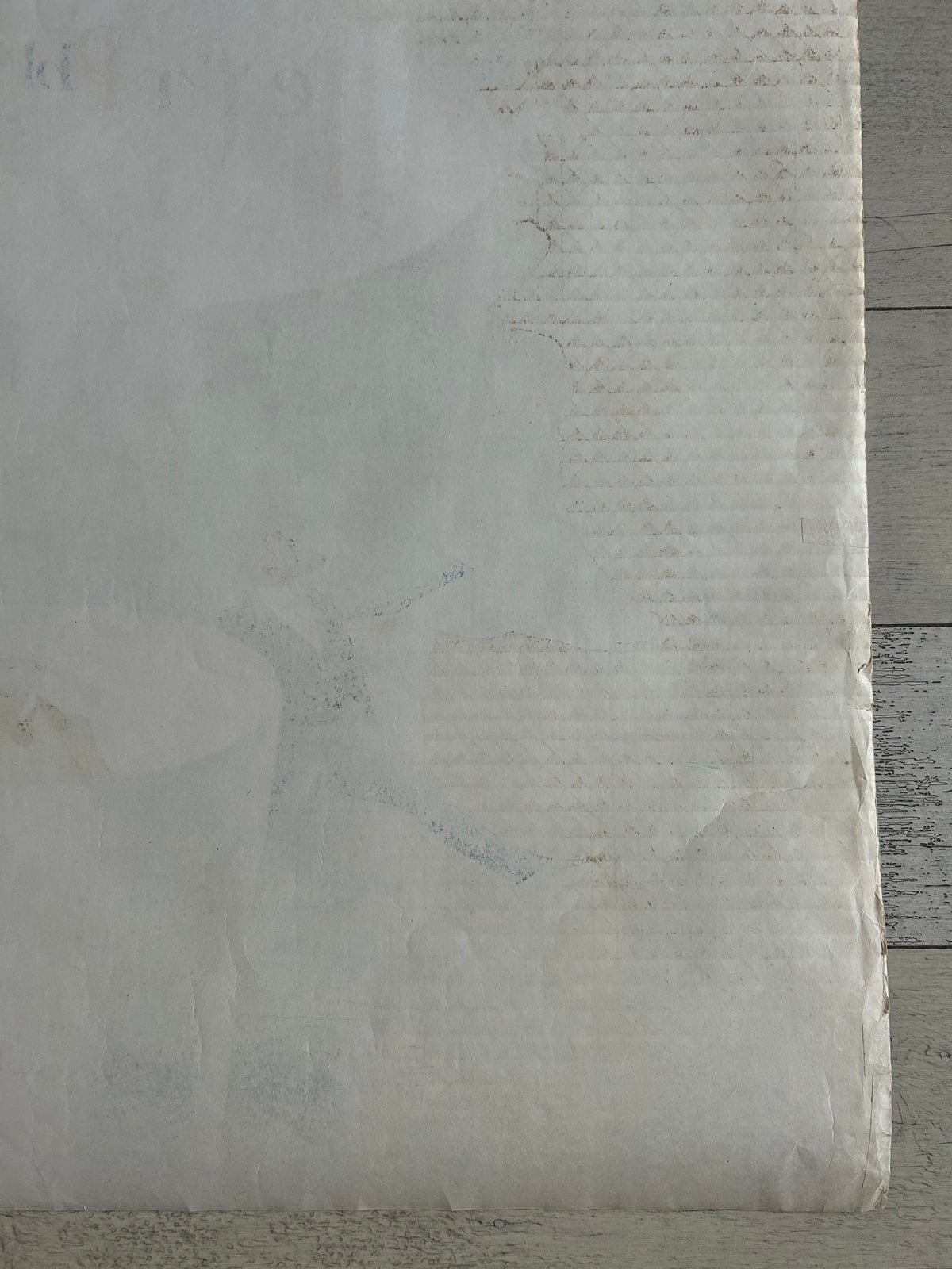 A close-up of a textured, off-white fabric or paper material with a subtle vertical ribbed pattern and faint gray markings, set against a weathered gray wood background.