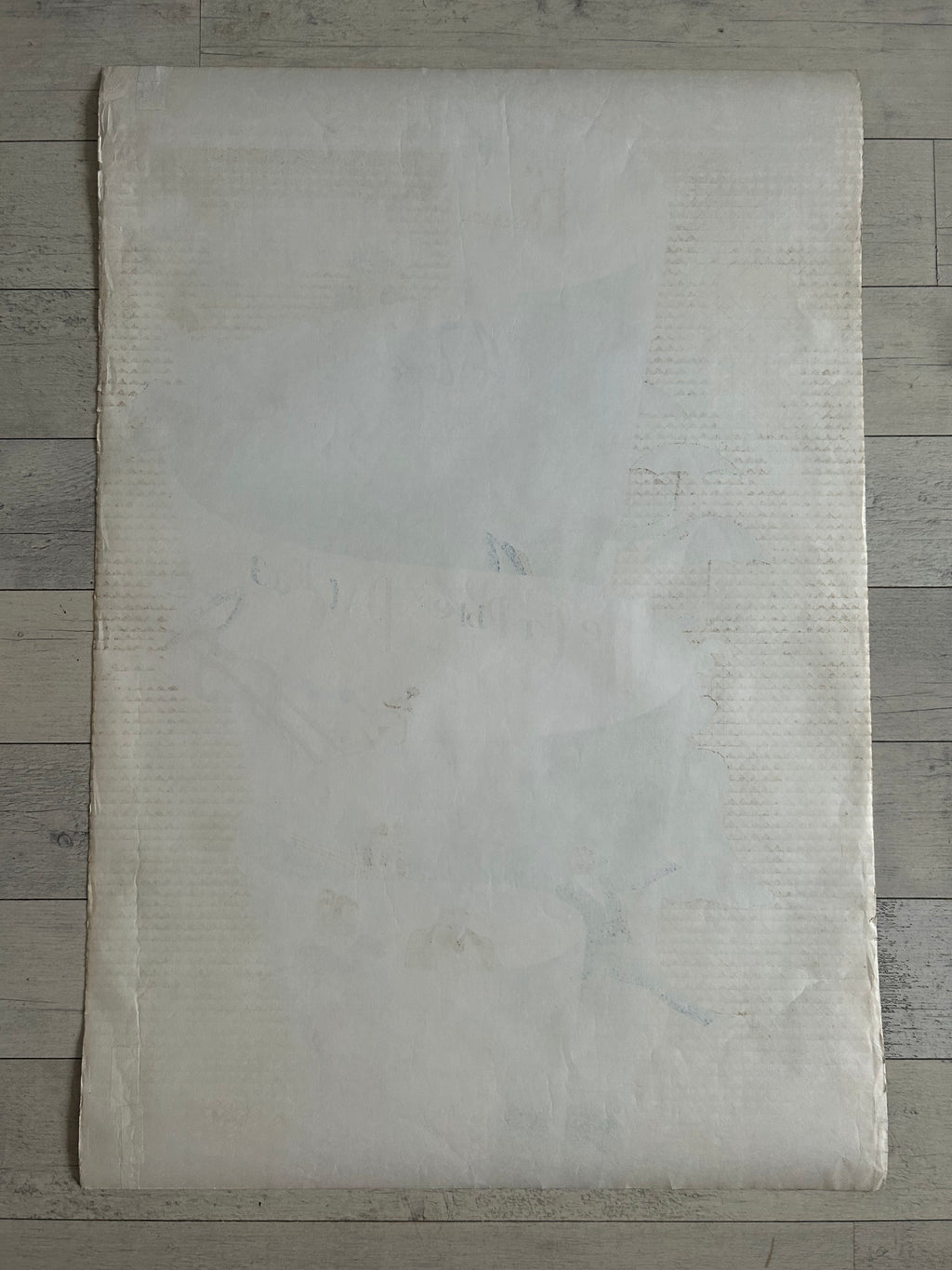 A large, flat, off-white textured sheet of paper or fabric laid flat on a gray wood plank background.
