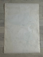 A large, flat, off-white textured sheet of paper or fabric laid flat on a gray wood plank background.