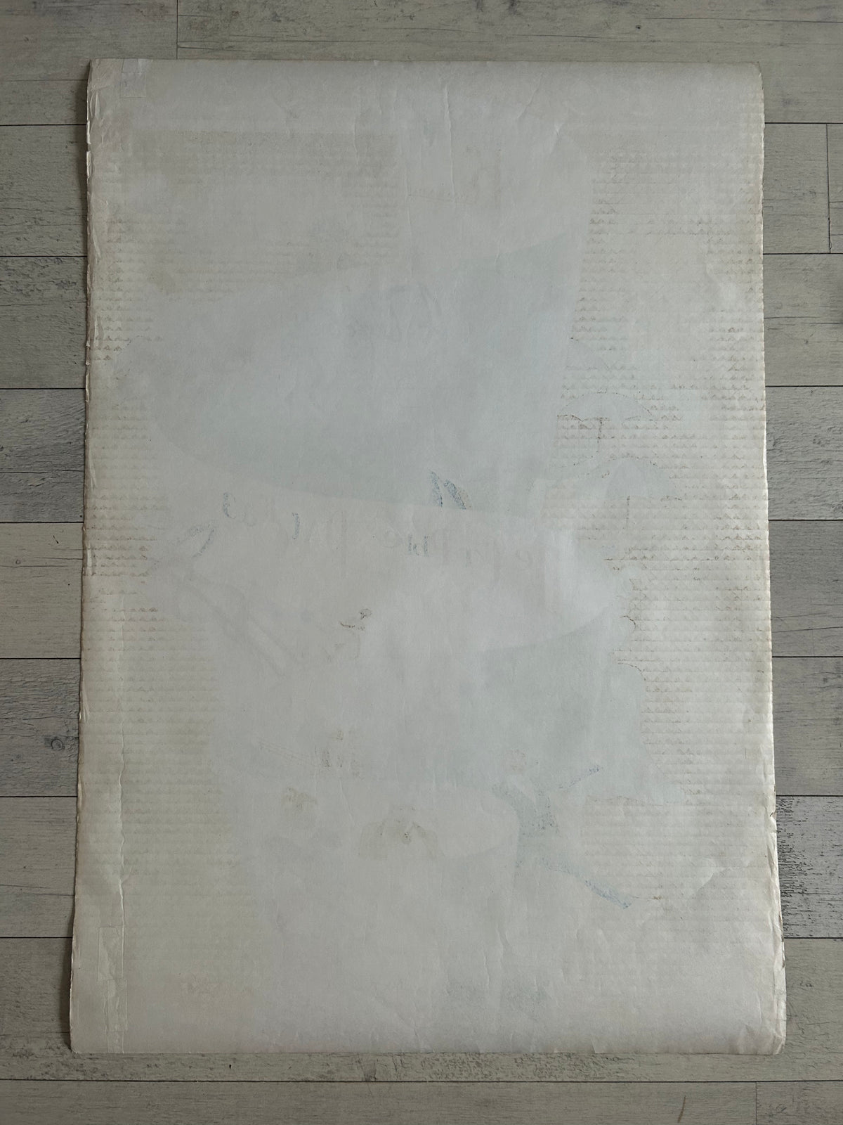 A large, flat, off-white textured sheet of paper or fabric laid flat on a gray wood plank background.