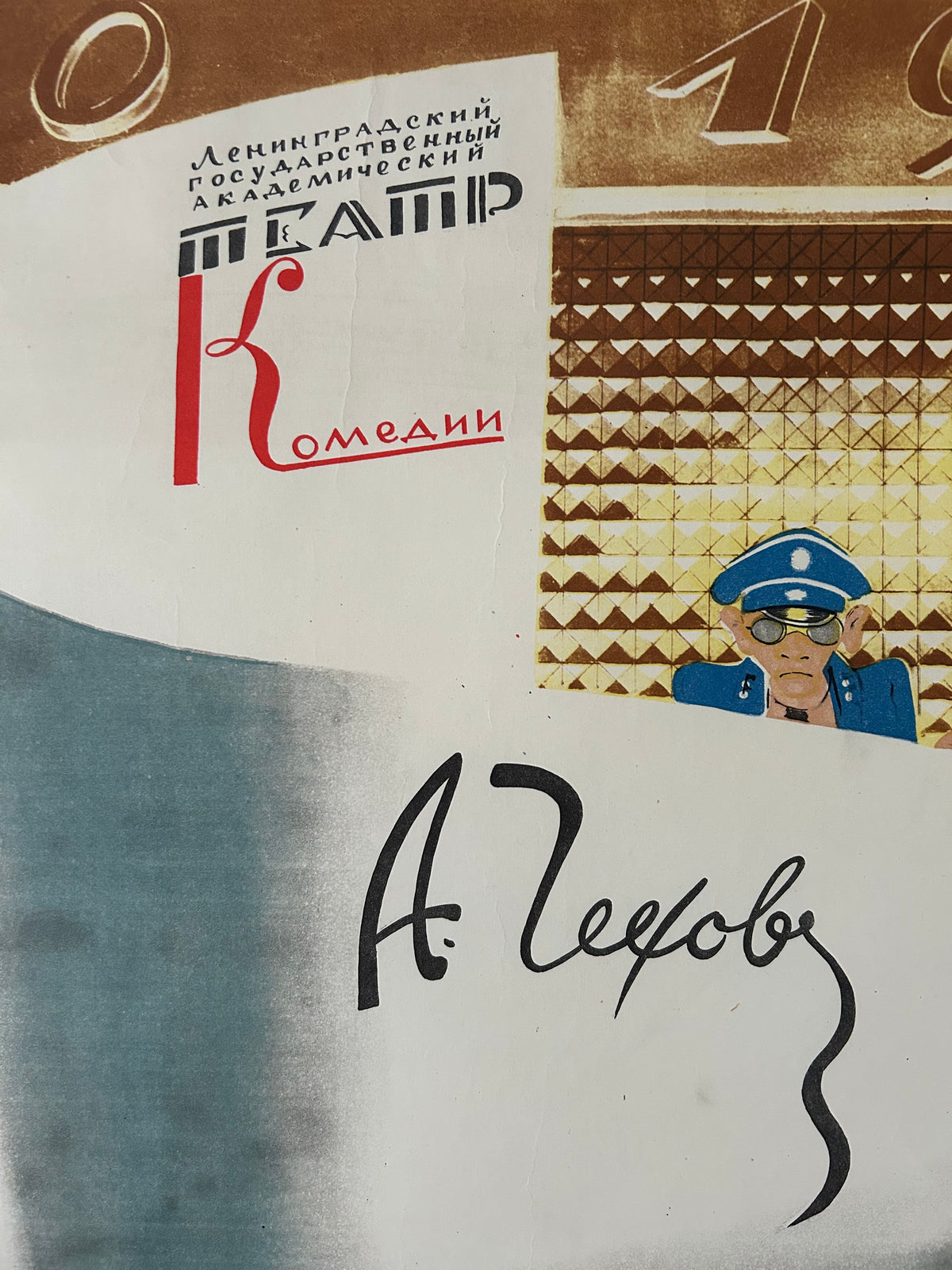 A close-up of a printed sign or poster with a white background, a brown geometric patterned section, a small illustration of a police officer in blue, Cyrillic text, and a large black cursive signature or word on the right.