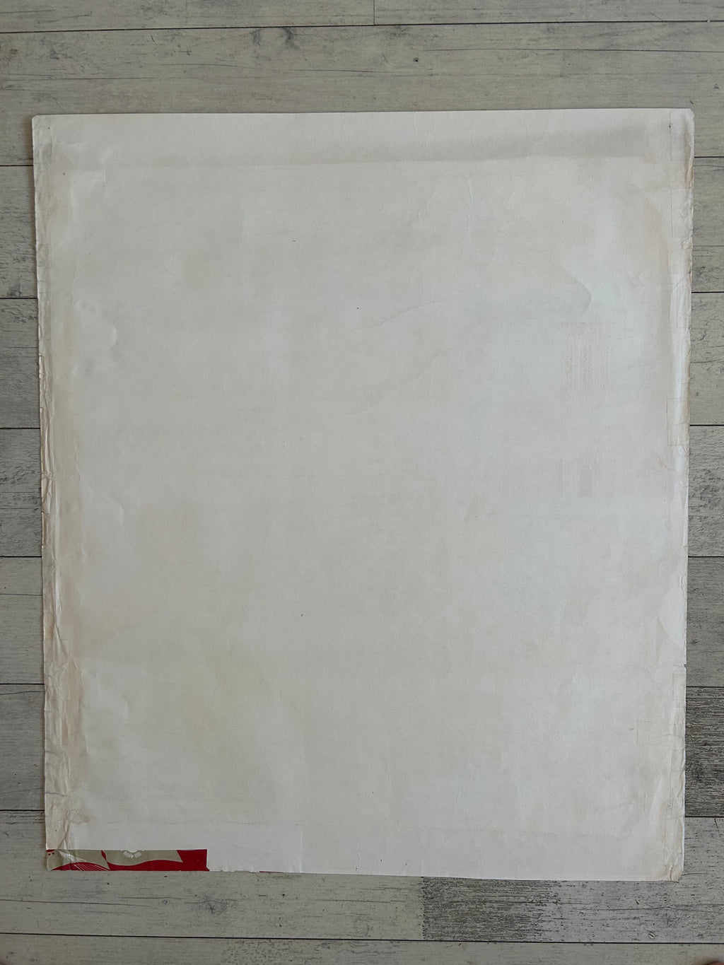 A large, blank off-white sheet of paper or cardstock laid flat on a gray wooden plank surface.