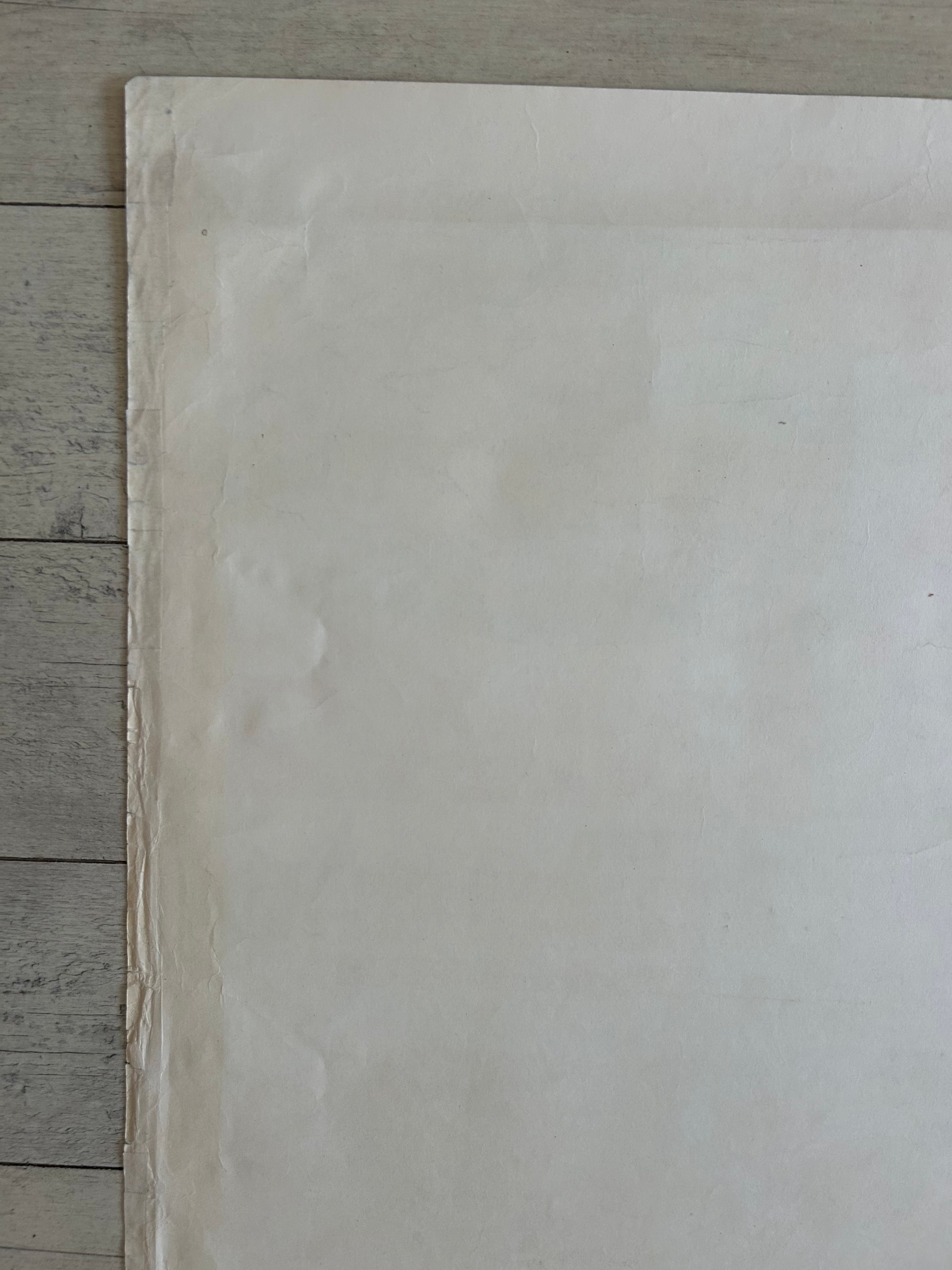 A large sheet of off-white paper or fabric laid flat on a light gray wood plank surface, with the top and right edges extending out of frame.