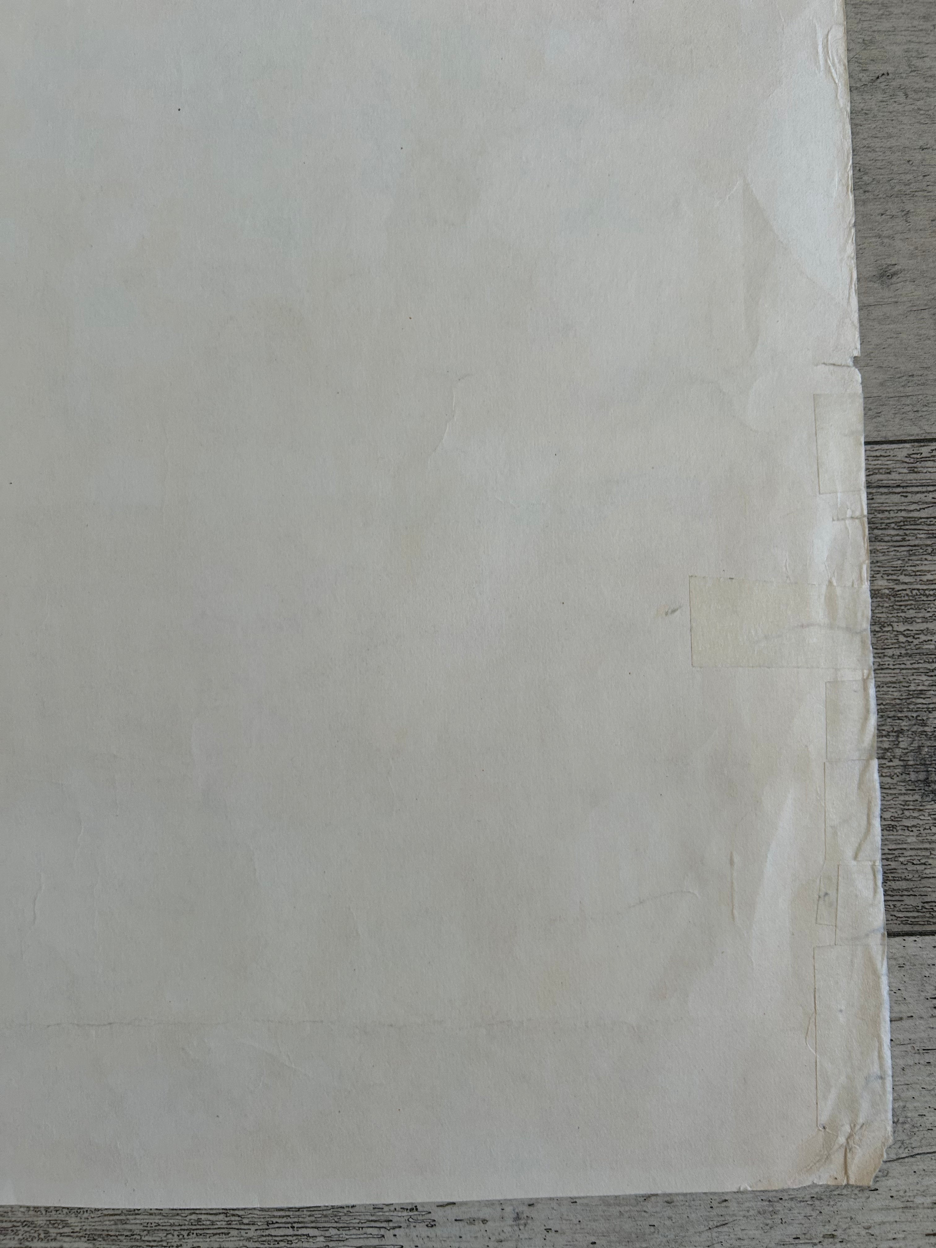 A close-up of a large off-white sheet of paper or fabric with a slightly textured surface, taped along one edge, resting on a gray wood surface.