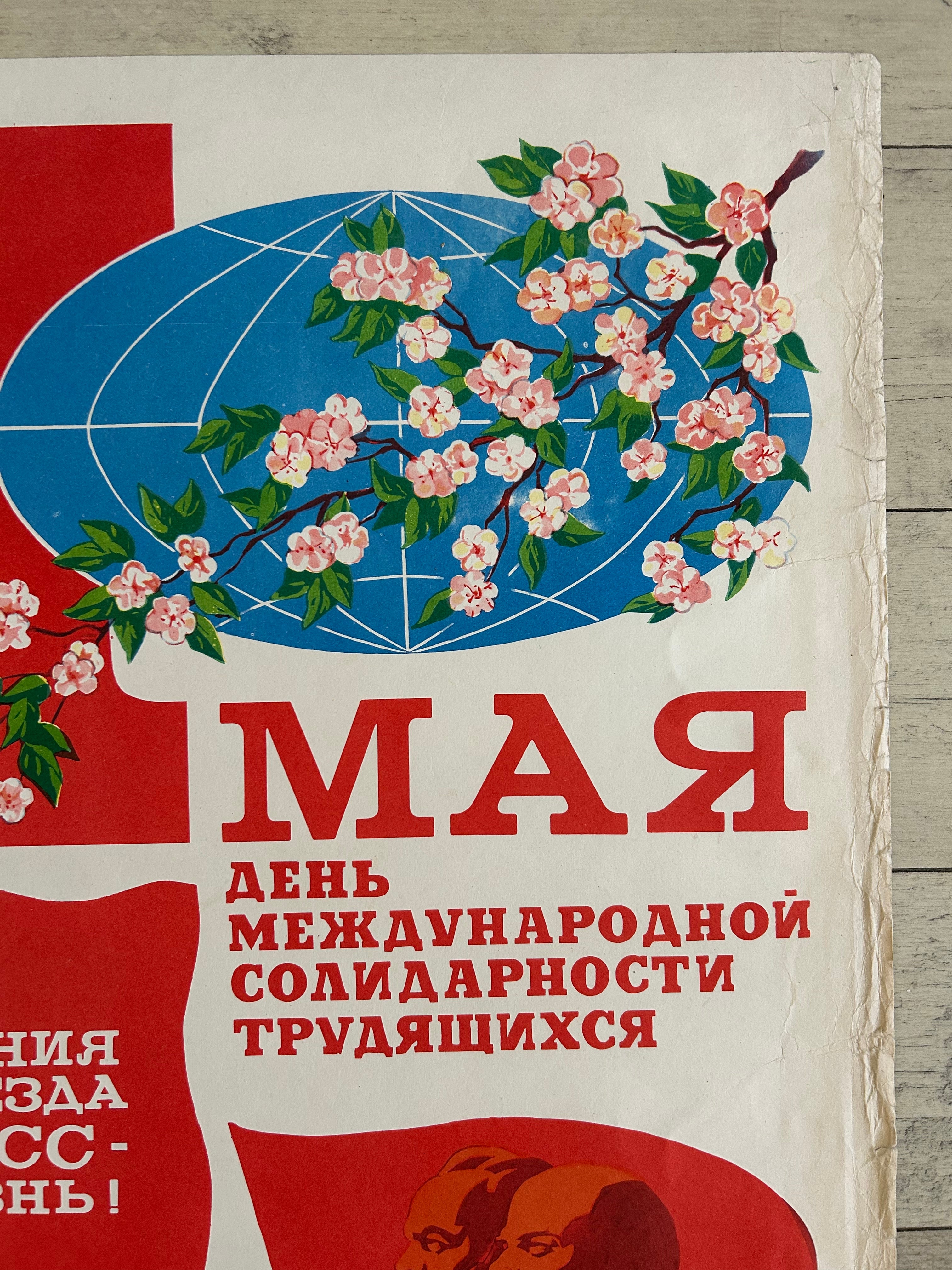 A vintage-style Soviet propaganda poster print featuring a blue globe with pink blossoms, large red Cyrillic text, and a red abstract shape on an off-white background, photographed against a light wood surface.