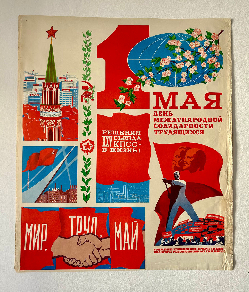 A vintage Soviet-style May Day propaganda poster with bold red, blue, and cream sections, featuring illustrations of a spire, flowers, a globe, flags, a worker, and a handshake. The Russian text reads '1 МАЯ' and other celebratory slogans.