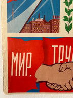 A close-up of a vintage Soviet propaganda poster print featuring a handshake, a cityscape with the word 'Leningrad', and large Cyrillic text on red and blue panels.