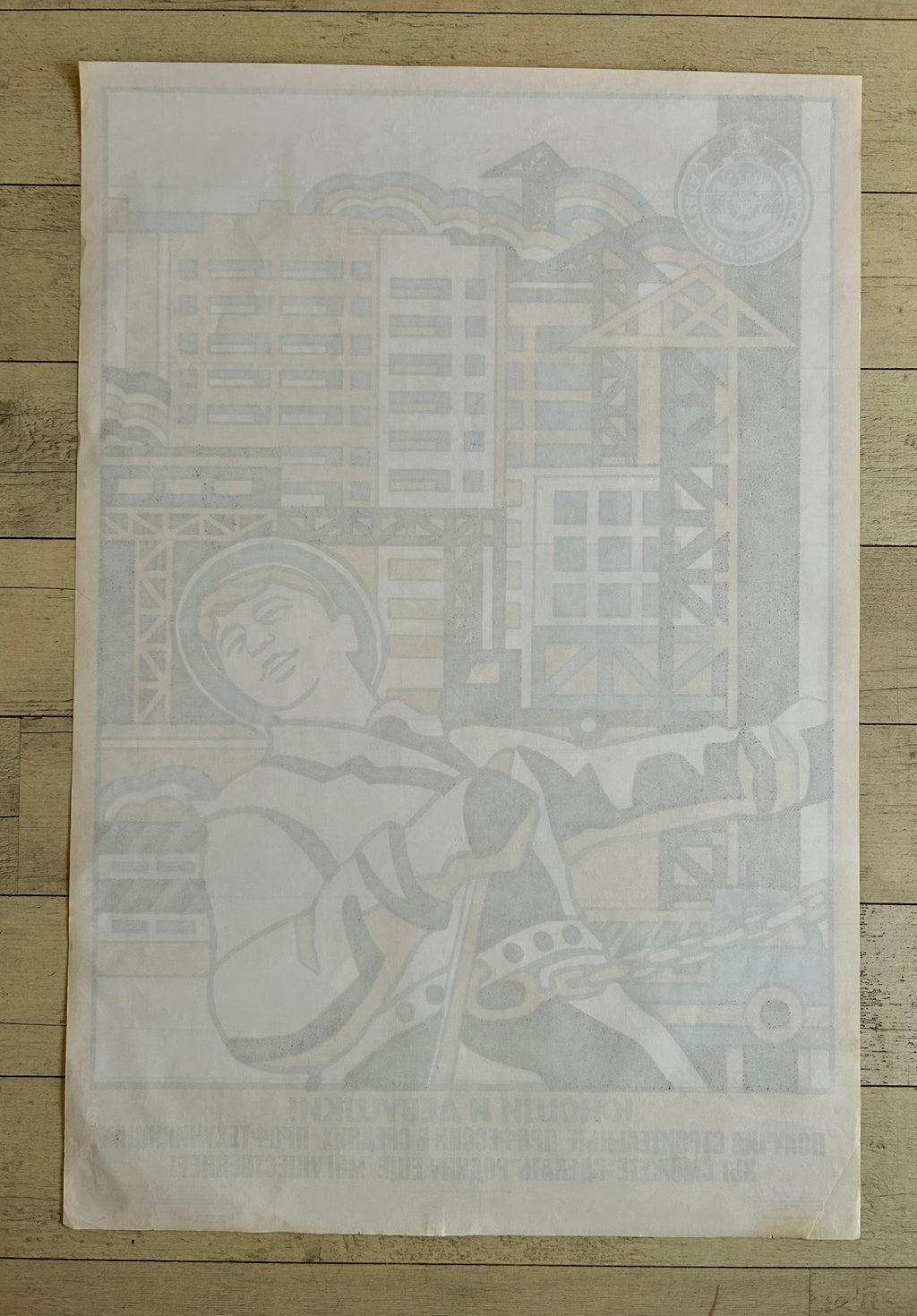 A vintage Soviet propaganda poster featuring a worker holding a hammer and sickle, with a city skyline in the background, displayed flat on a light wooden surface.