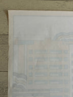 A close-up of a light beige paper sheet with faint pale blue and gray printed architectural or geometric line art, placed on a weathered wood surface.