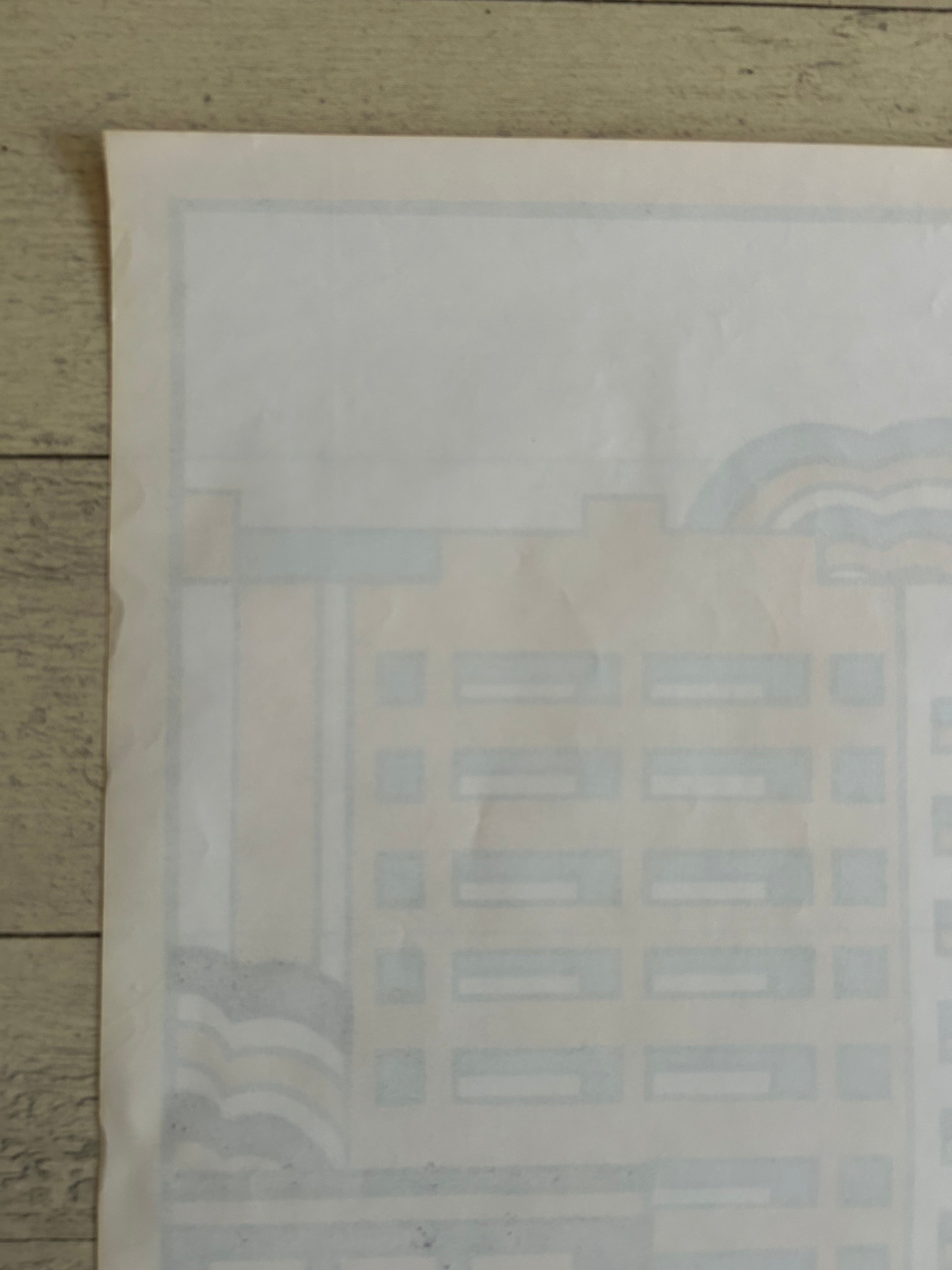 A close-up of a light beige paper sheet with faint pale blue and gray printed architectural or geometric line art, placed on a weathered wood surface.