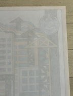 A close-up of a printed poster or art print laid on a light wood surface, showing a faint architectural illustration with a circular emblem in the upper right.
