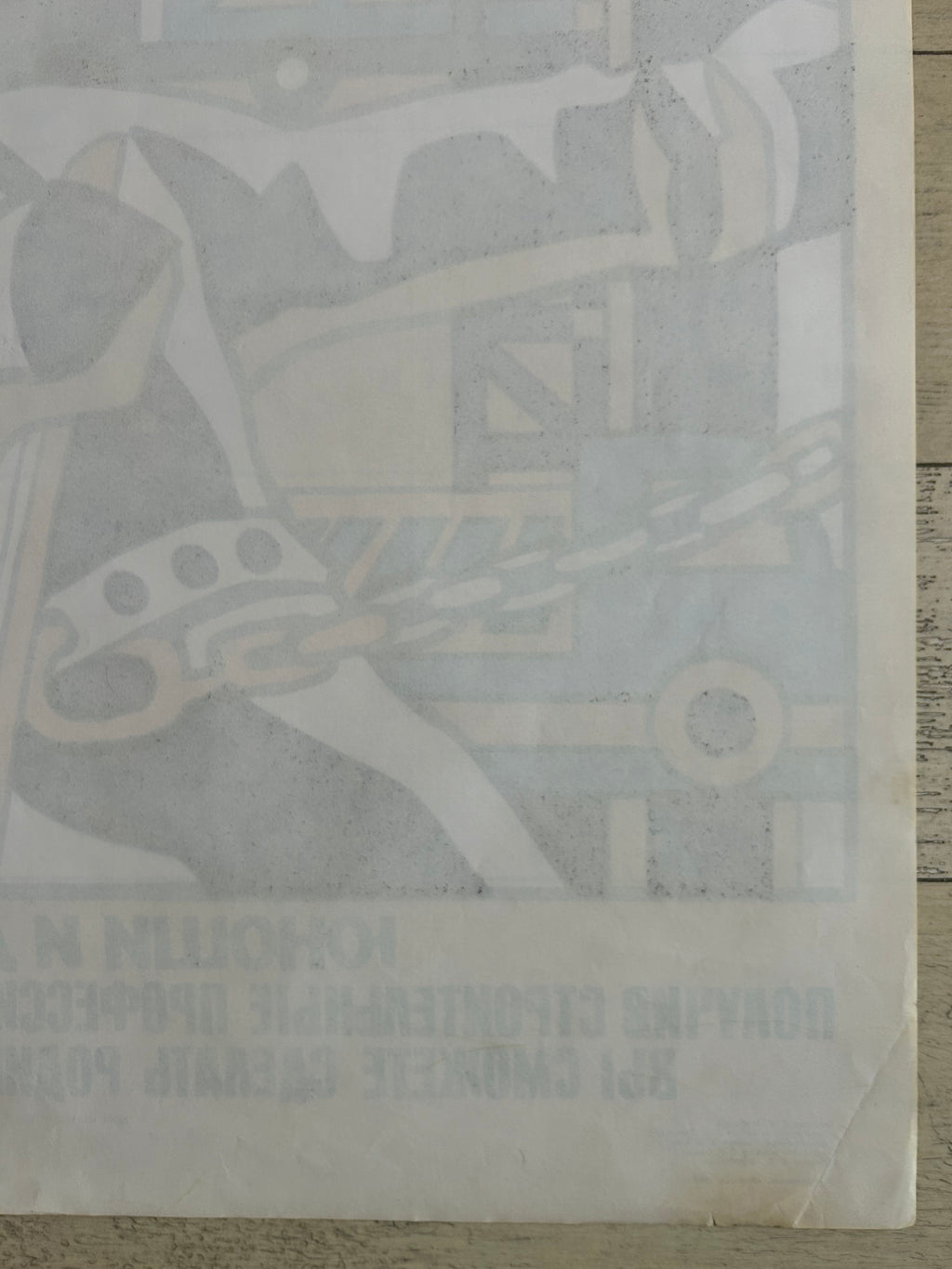 A vintage Soviet propaganda poster depicting a construction scene with a hammer and chain, printed in muted blue-gray and beige tones on aged off-white paper, laid flat on a light wood surface.