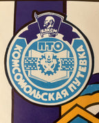 A close-up of a circular Soviet youth emblem in blue, white, and purple, featuring Cyrillic text and a central gear-and-sickle symbol.