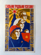 A vintage Soviet-style propaganda poster print mounted on a white wall. The poster features three stylized faces in blue, yellow, red, and white, with Cyrillic text at the top and industrial motifs in the border.