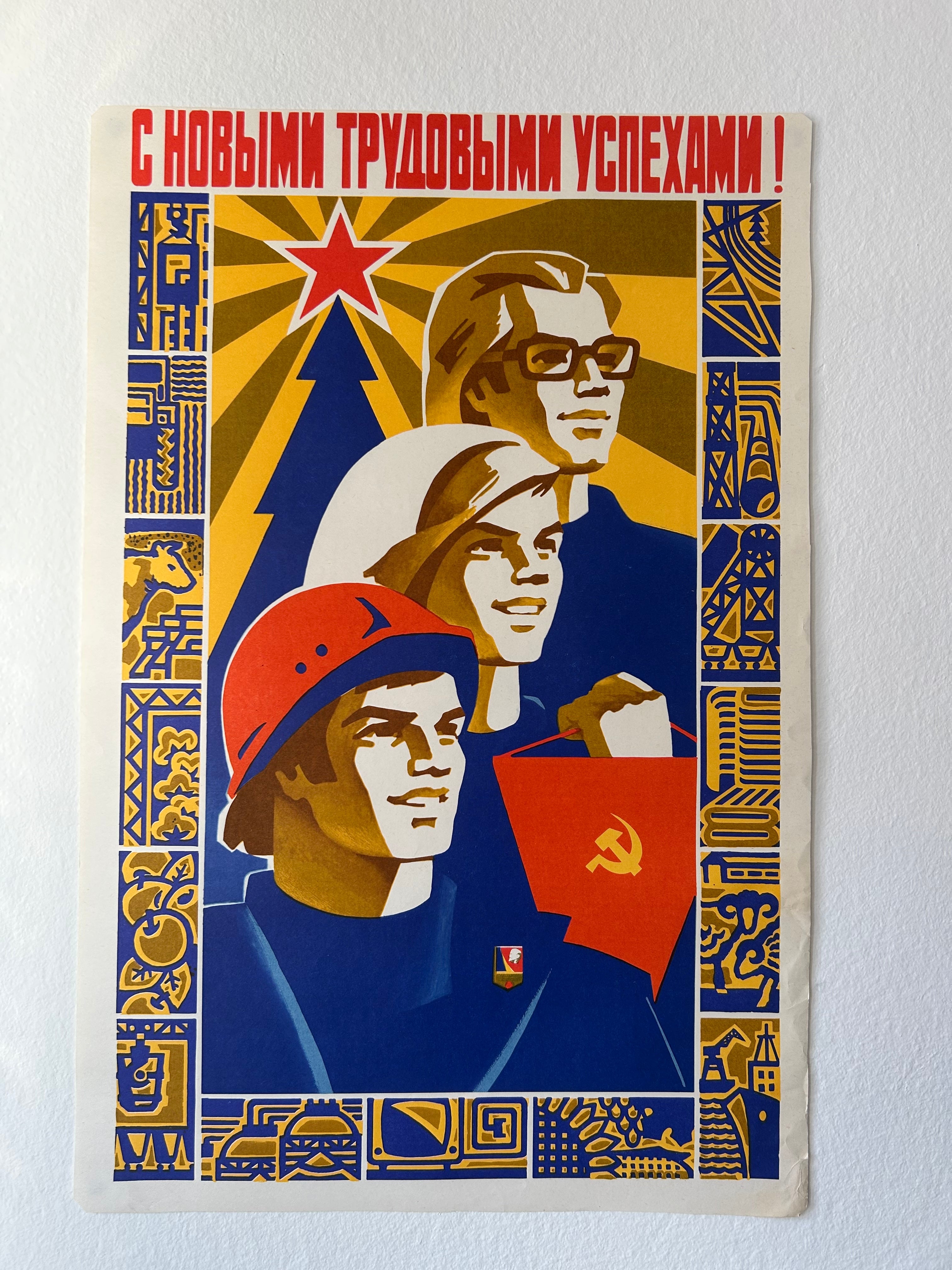 A vintage Soviet-style propaganda poster print mounted on a white wall. The poster features three stylized faces in blue, yellow, red, and white, with Cyrillic text at the top and industrial motifs in the border.