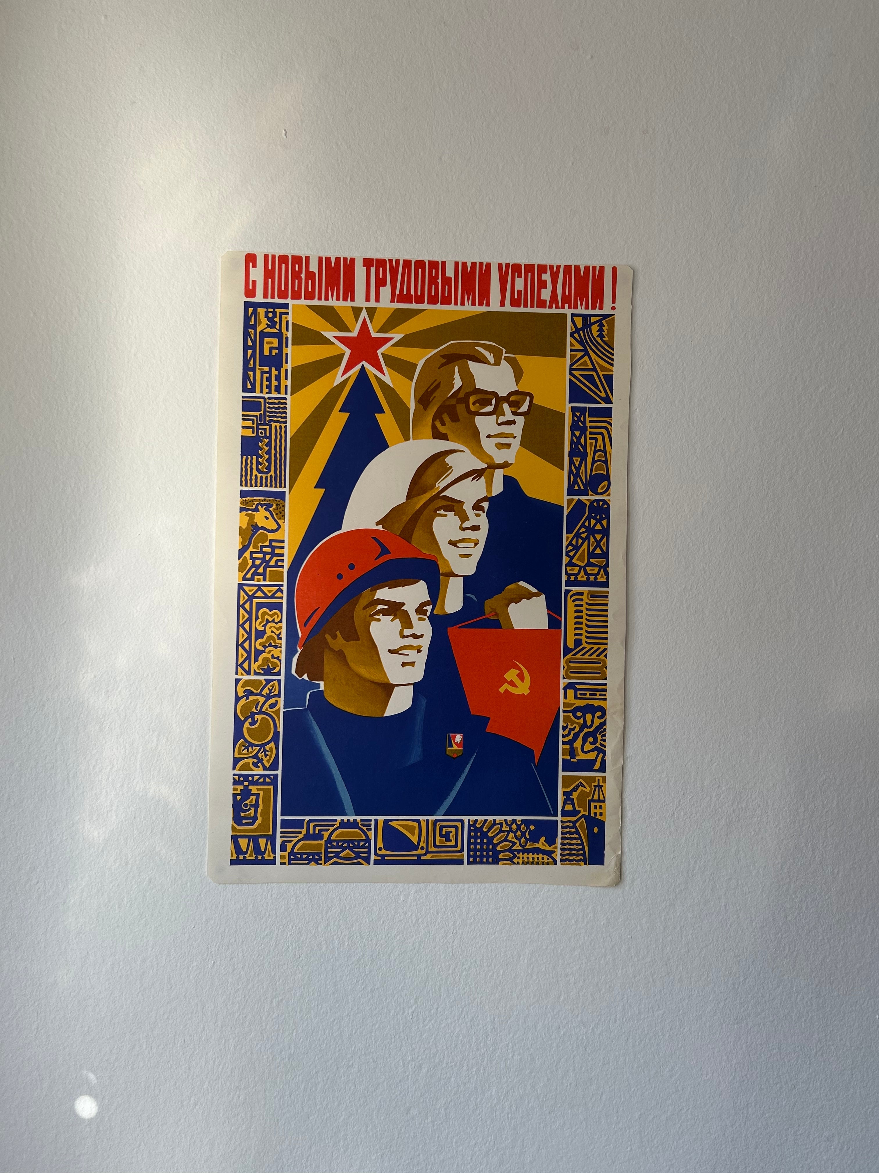 A vintage Soviet propaganda poster print featuring three stylized workers with red stars and blue uniforms, mounted on a light gray wall.
